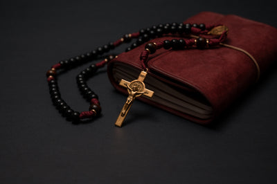 Handmade St. Benedict paracord rosary in burgundy cord with black wood beads, draped over a leather journal