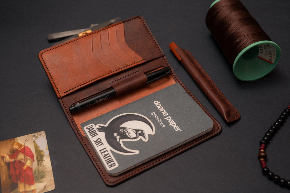 Two-tone full grain leather pocket journal cover open, showing card slots, a pen in the pen loop, and a pocket notebook
