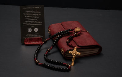 The Protector paracord rosary displayed with a Prayer of St. Benedict card